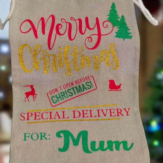 Personalised Christmas gift sack for Mum – hessian bag with red, gold, and green festive vinyl design, “Merry Christmas” text, reindeer and sleigh icons, and special delivery message, with soft Christmas tree background.