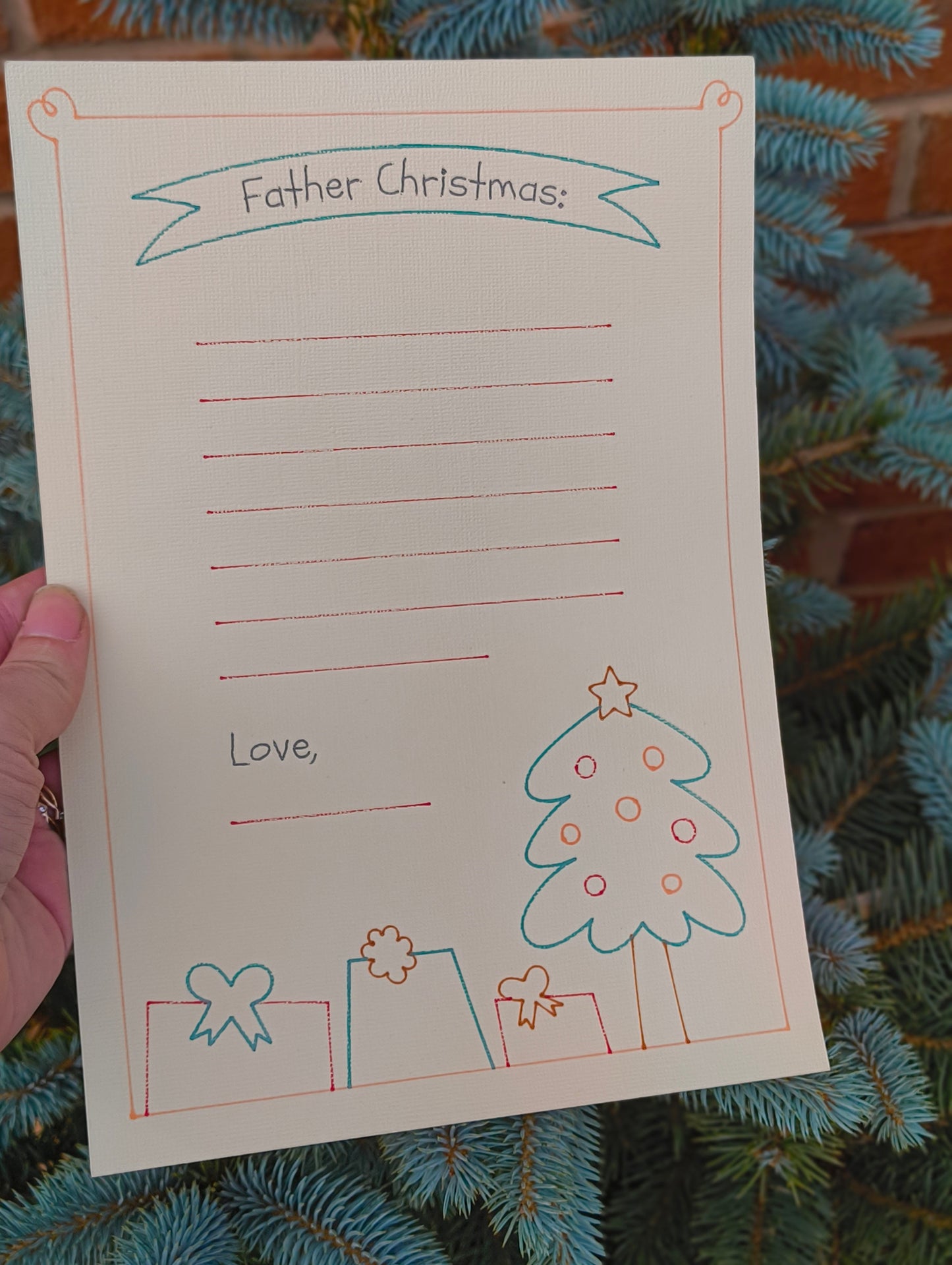 Close-up of Father Christmas letter writing paper held in hand with festive tree background.