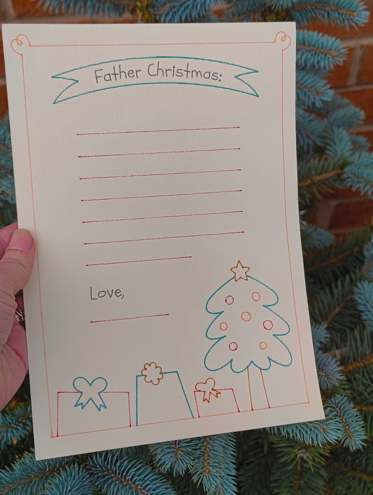 Close-up of Father Christmas letter writing paper held in hand with festive tree background.