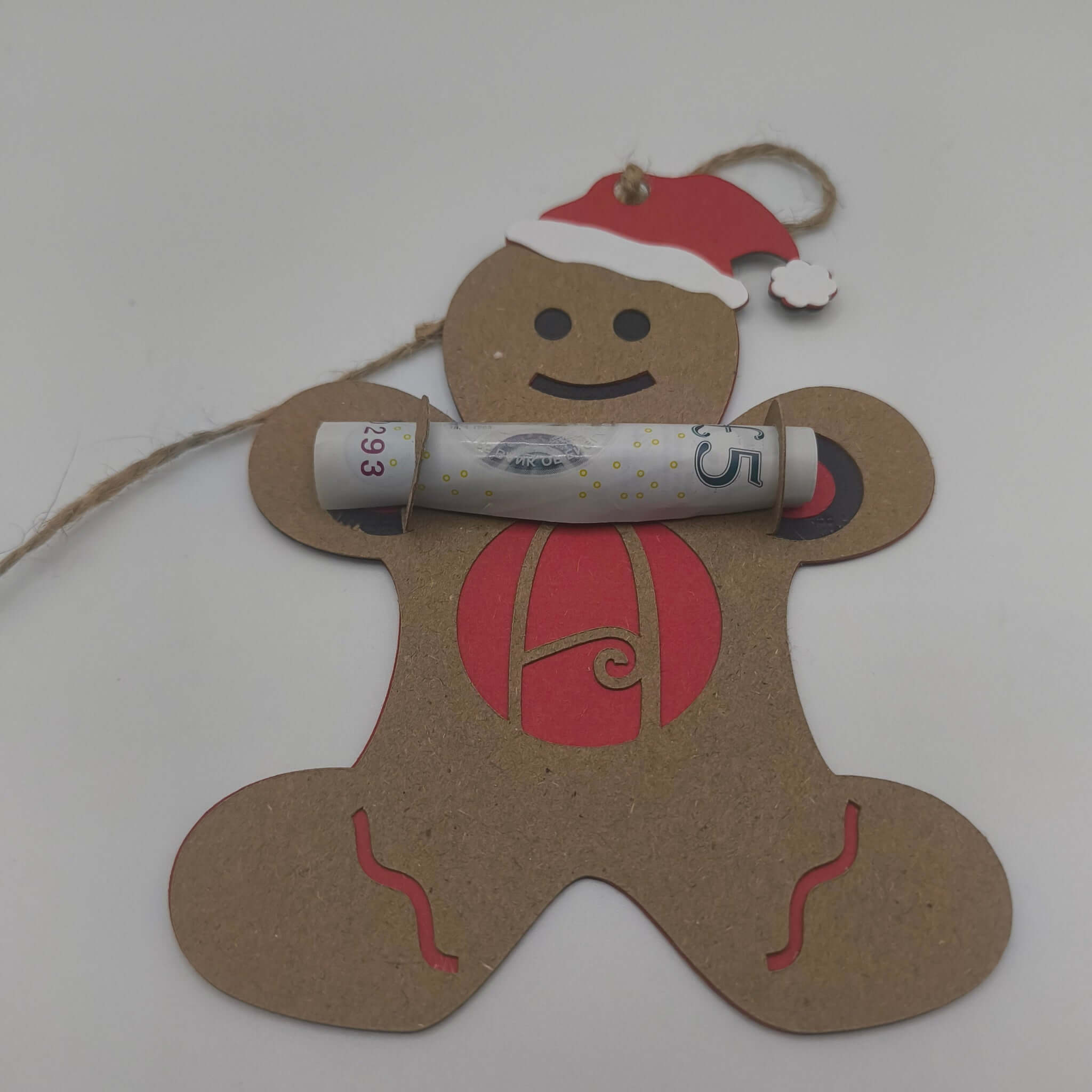 Gingerbread man money holder ornament holding a rolled £5 note, with red and kraft card layers and Santa hat detail.