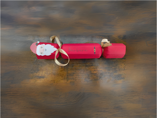 Handmade red Christmas cracker with Santa face, gold ribbon, and personalised name in script text, displayed on rustic wooden background.
