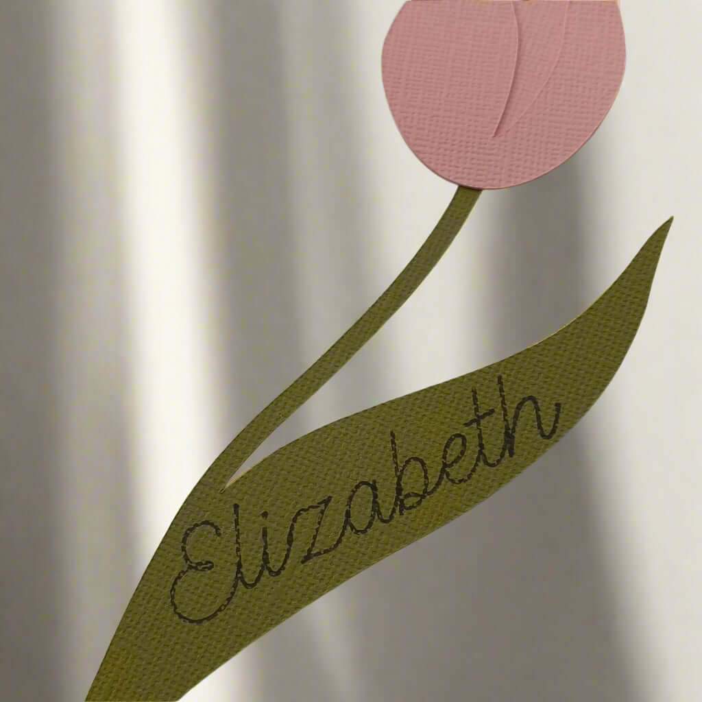 Close-up of a tulip place card showing the name “Elizabeth” in cursive on the leaf, textured cardstock design in pink and green.