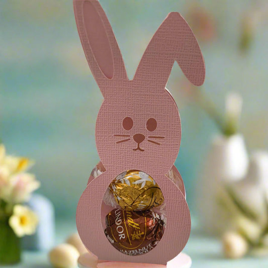 Handmade pink bunny Easter treat holder with chocolates inside, styled with pastel Easter eggs on a spring table.