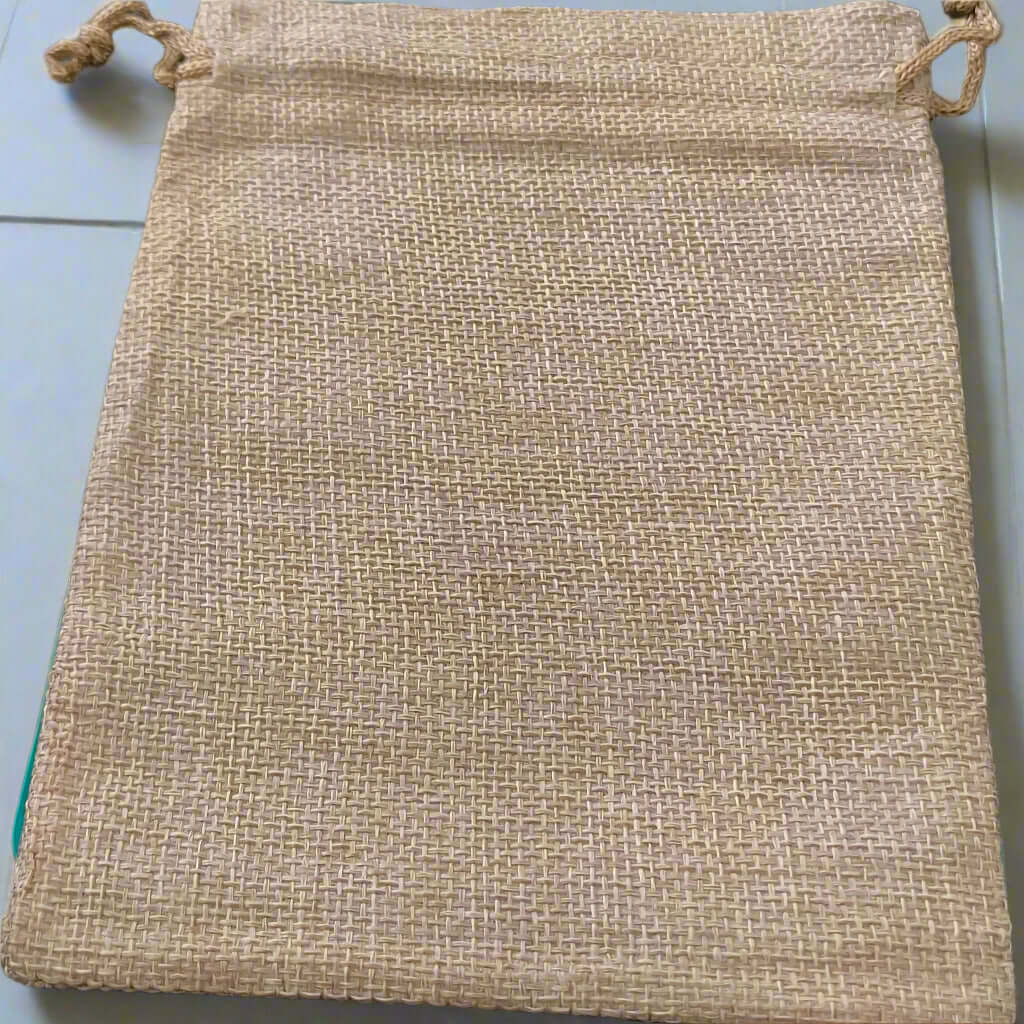 Plain burlap drawstring gift bag laid flat on a light surface, showing the natural woven texture of the fabric with no visible design or text.