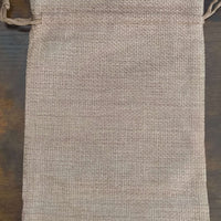Plain hessian drawstring gift bag displayed on a dark wooden surface, showing the natural woven texture and rustic appearance without any printed design.