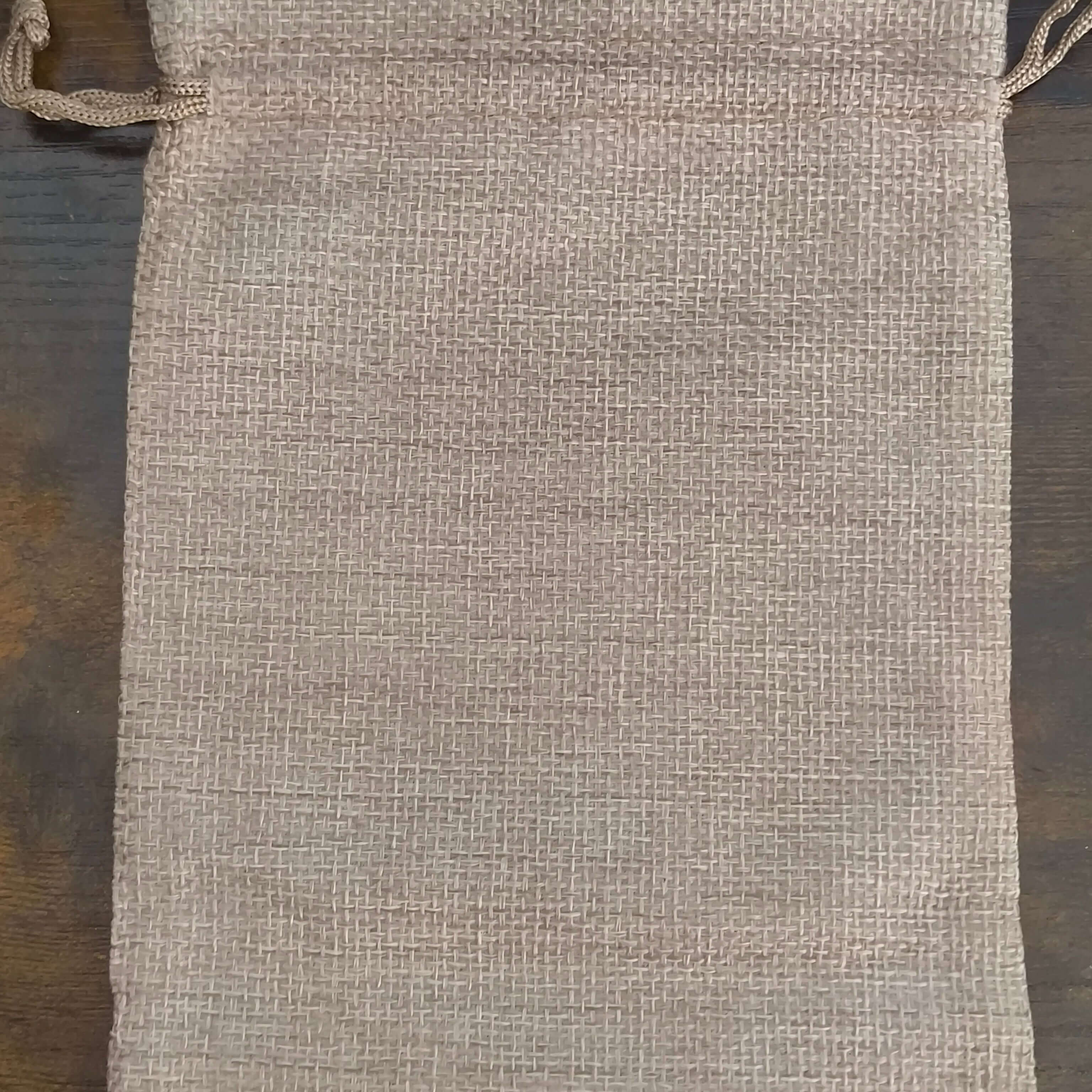 Plain hessian drawstring gift bag displayed on a dark wooden surface, showing the natural woven texture and rustic appearance without any printed design.