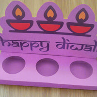 “Top-front angled photo of a handmade purple Diwali sweet holder with ‘Happy Diwali’ text and three red diya motifs, displayed on a wooden surface.”