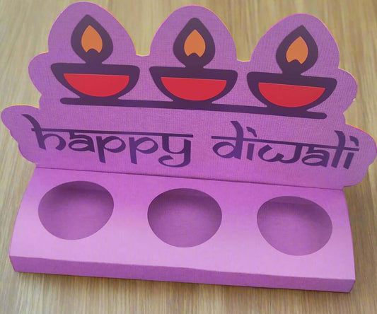 “Top-front angled photo of a handmade purple Diwali sweet holder with ‘Happy Diwali’ text and three red diya motifs, displayed on a wooden surface.”