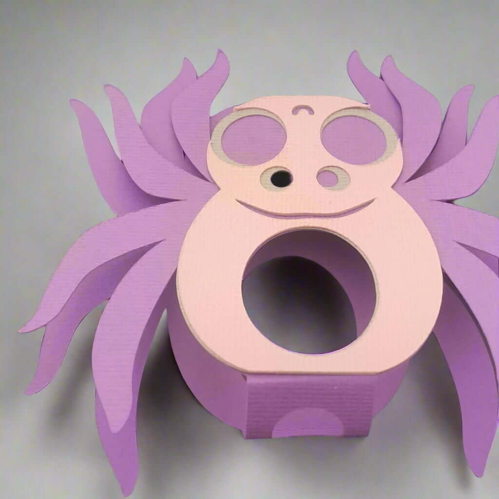 Handmade purple and pink paper spider lollipop holder with smiling face, featuring curved legs and textured cardstock, ideal for Halloween party favours or kids' treats.