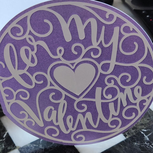Close view of lilac round Valentine’s card featuring decorative white swirls and a heart cut-out, emphasising the smooth cardstock texture and delicate craft detail.