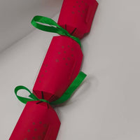 Red handmade Christmas cracker with green ribbon bows and embossed star pattern.