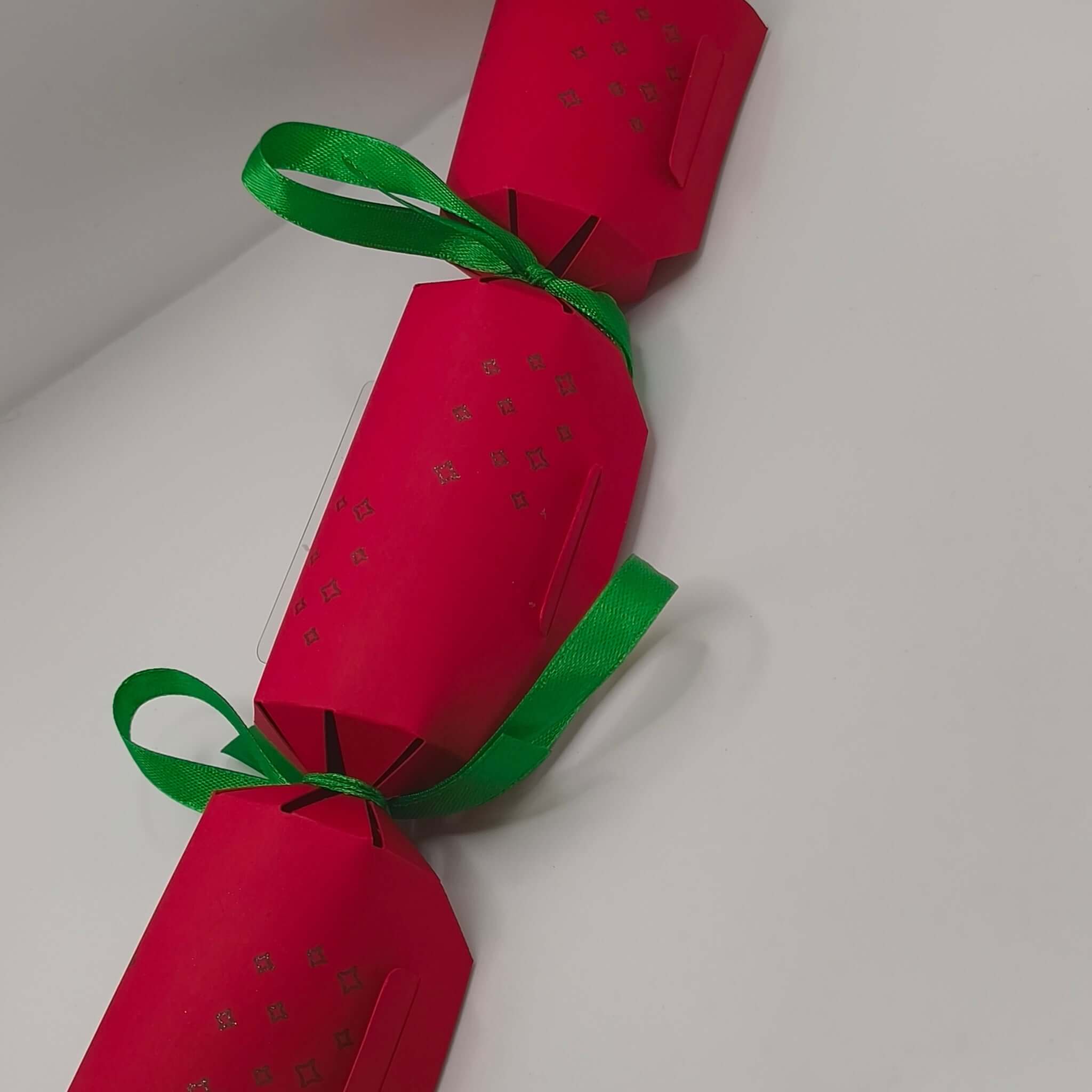 Red handmade Christmas cracker with green ribbon bows and embossed star pattern.