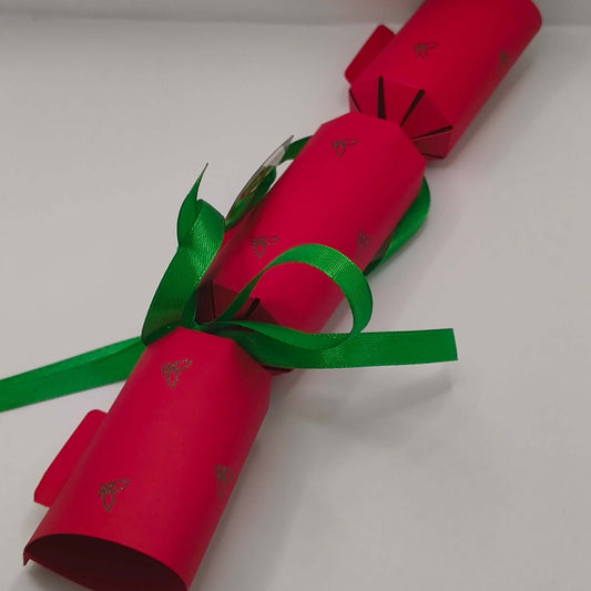 Red Christmas cracker decorated with small holly motifs and green ribbon bows.