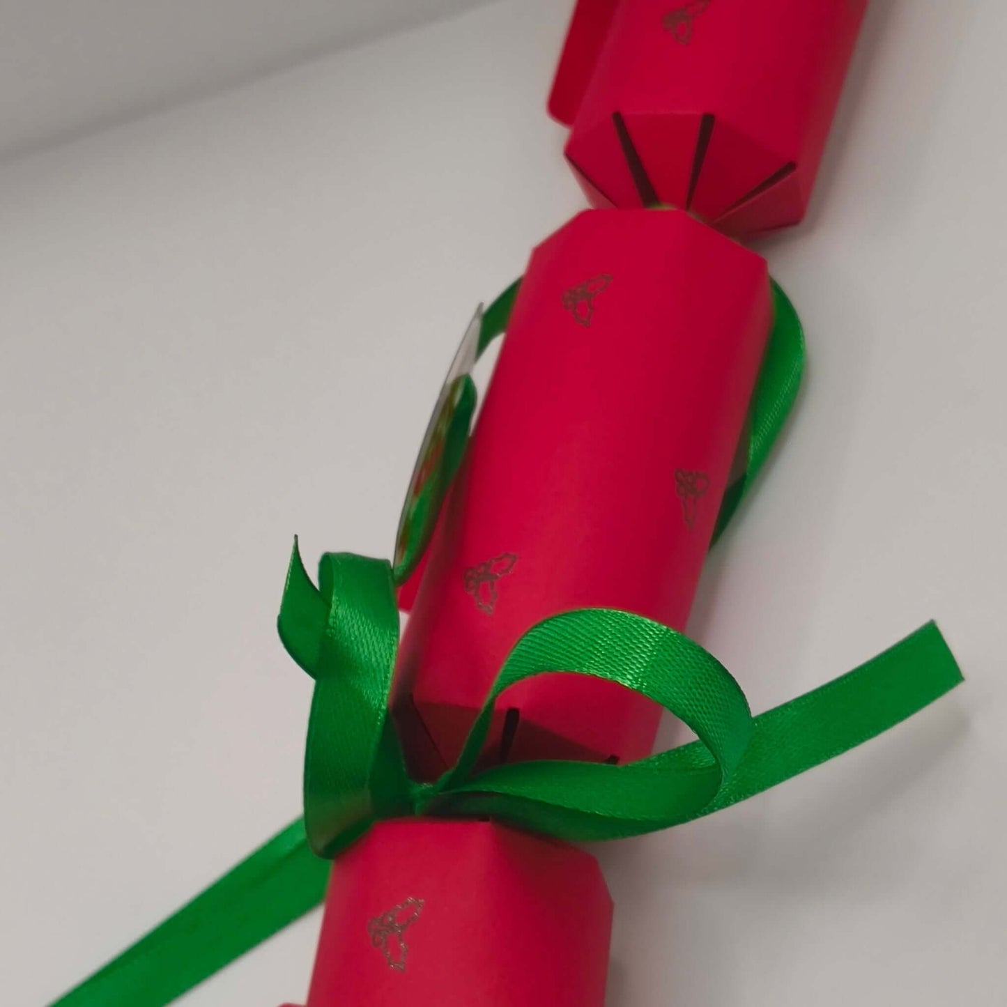 Side view of red cracker with green satin ribbon and silver holly print design.