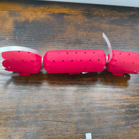 Plain red Christmas cracker with dotted cut-out design and scalloped edges, tied with silver ribbon, placed on wooden tabletop.