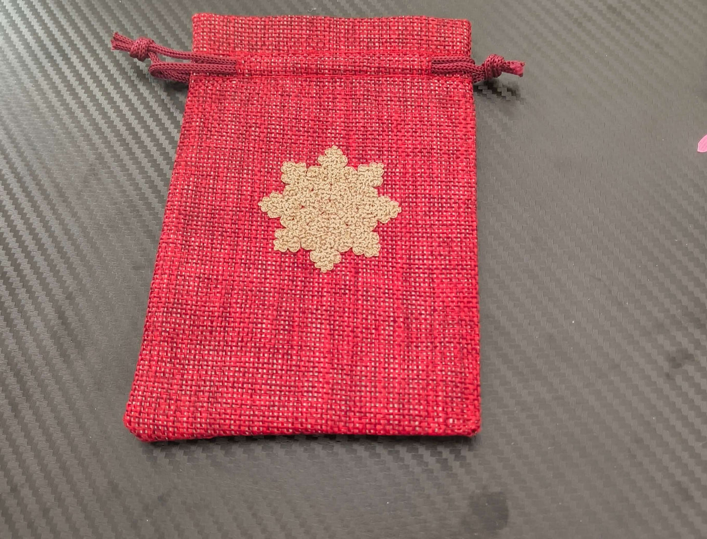 Red drawstring pouch with golden snowflake design, perfect for Christmas gift wrapping.