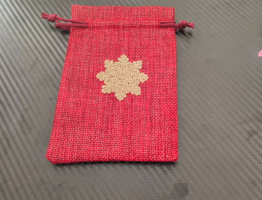 Red drawstring pouch with golden snowflake design, perfect for Christmas gift wrapping.