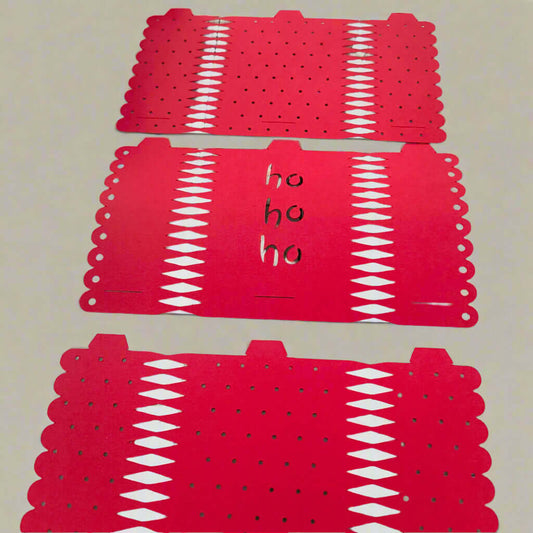 Three flat red paper Christmas cracker templates with decorative edge cuts and punched holes, one featuring handwritten 'ho ho ho' in the centre, displayed on a neutral background.