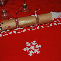 Single kraft reindeer cracker with antlers, red nose, and “Steve” in gold lettering, tied with pink ribbon and placed on a red snowflake placemat.