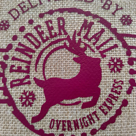 Detailed view of burgundy reindeer motif on rustic hessian Christmas gift bag with festive lettering.