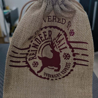 Standing hessian gift bag tied with drawstring, featuring "Reindeer Mail Overnight Express" festive burgundy design.