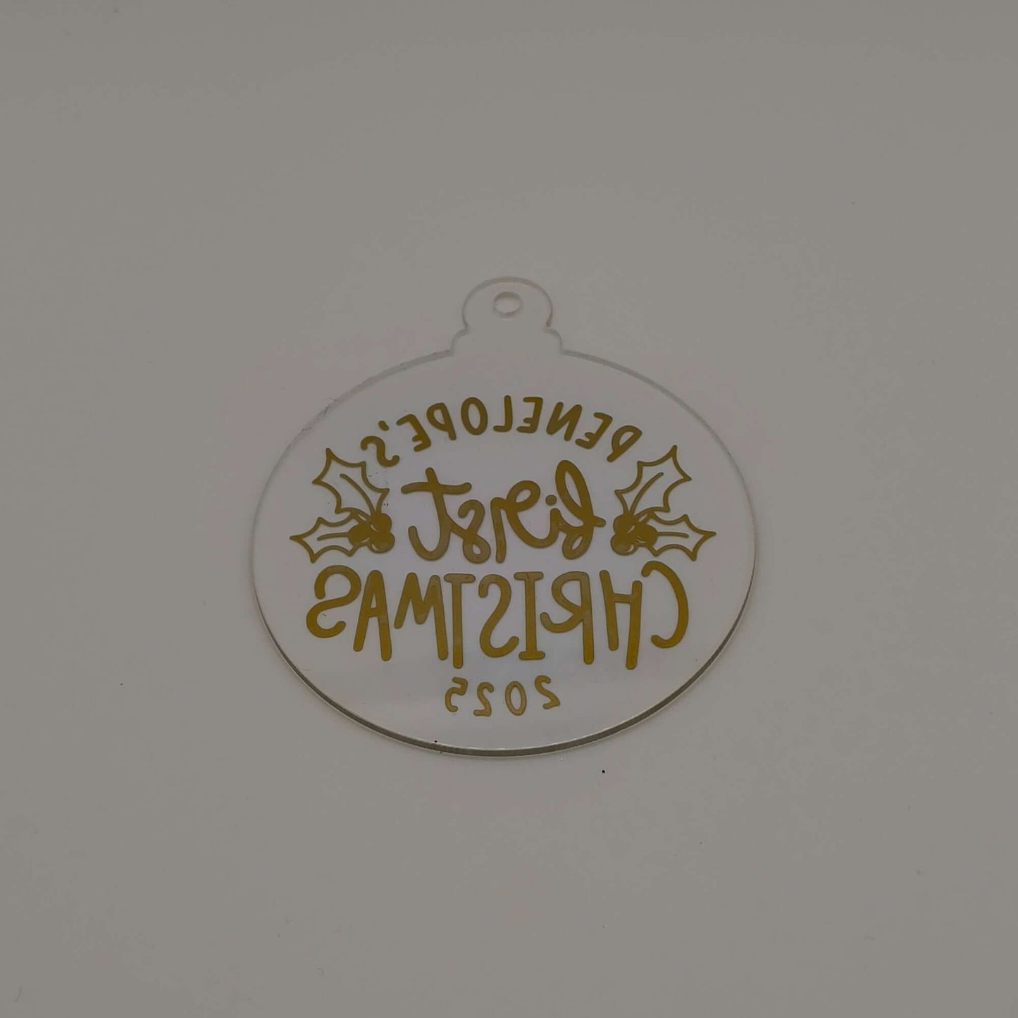 Reverse view of personalised gold and clear acrylic first Christmas bauble showing text from back.