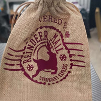 Rustic Christmas hessian bag with burgundy reindeer design, closed at the top with drawstring.