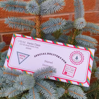Personalised Santa delivery envelope with festive design resting on a Christmas tree.