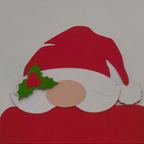 Close-up of handmade Santa money holder card, showing the red hat, white beard, and green holly detail with a festive berry on a plain background.