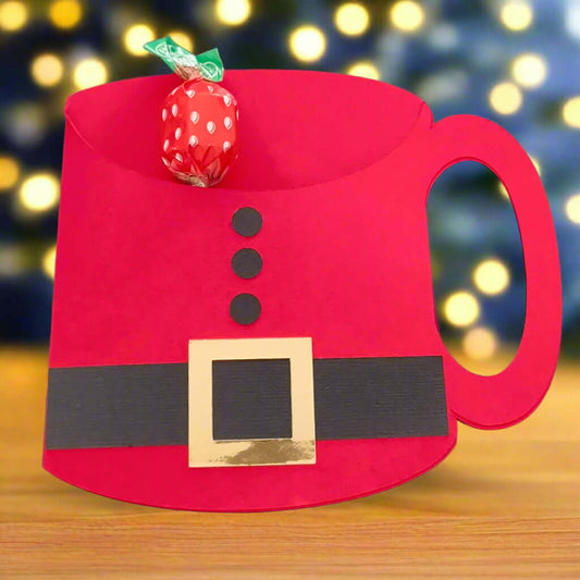 Handcrafted Santa suit mug-shaped gift card holder displayed on a wooden table with blurred Christmas lights in the background – perfect for festive gifting, stocking fillers, or table favours – chocolates not included.