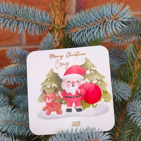 Close-up of Santa and reindeer coaster, personalised with name and year, resting among festive evergreen branches.