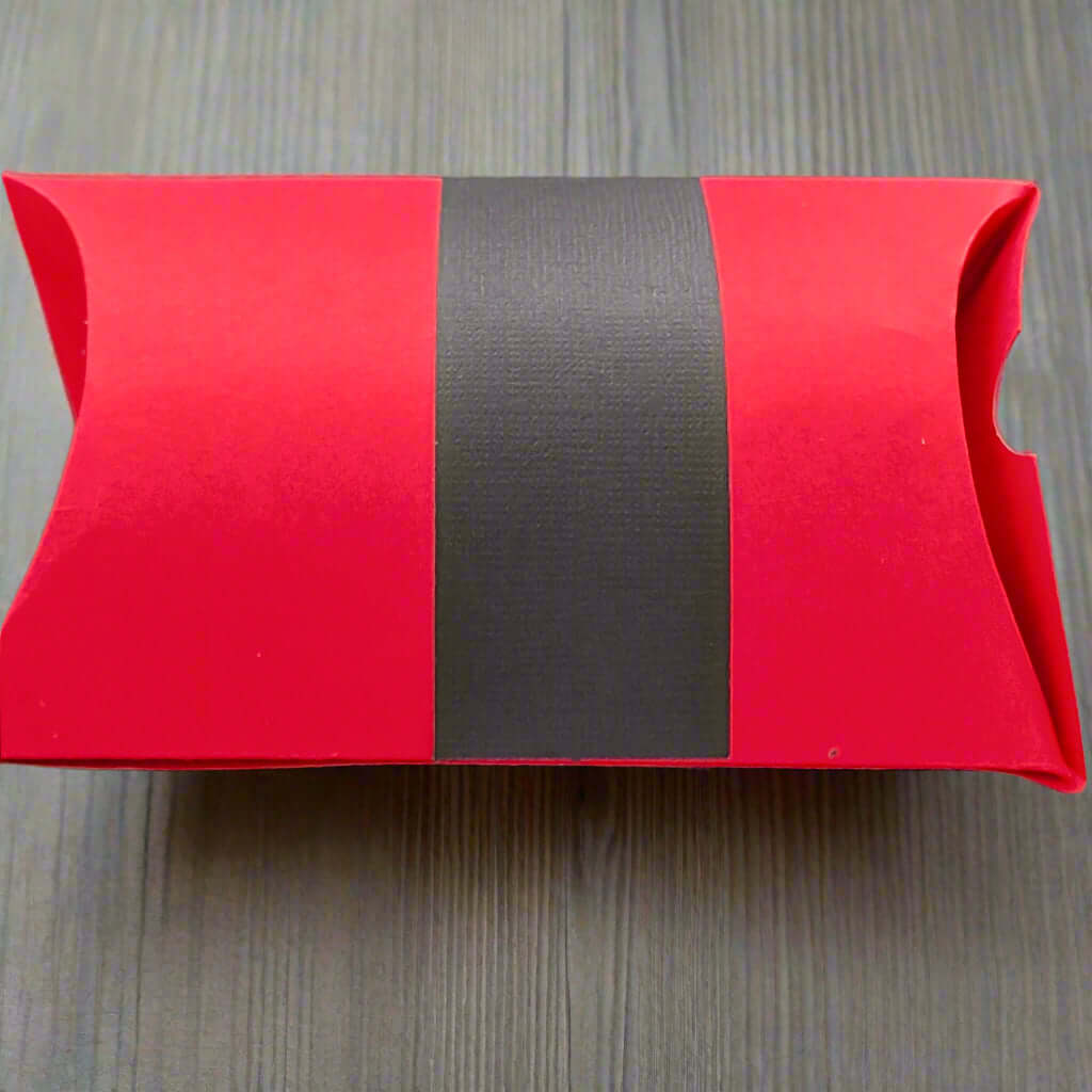 Back view of a handmade red Christmas pillow gift box with a wide black belt design, displayed on a light wood grain background for a clean and festive presentation.
