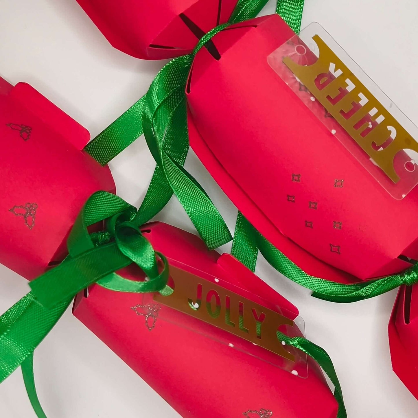 Set of red Christmas crackers with gold ‘CHEER’ and ‘JOLLY’ tags tied with green ribbons.