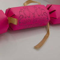 Personalised Birthday Crackers in vibrant pink with happy birthday design and gold ribbon details.