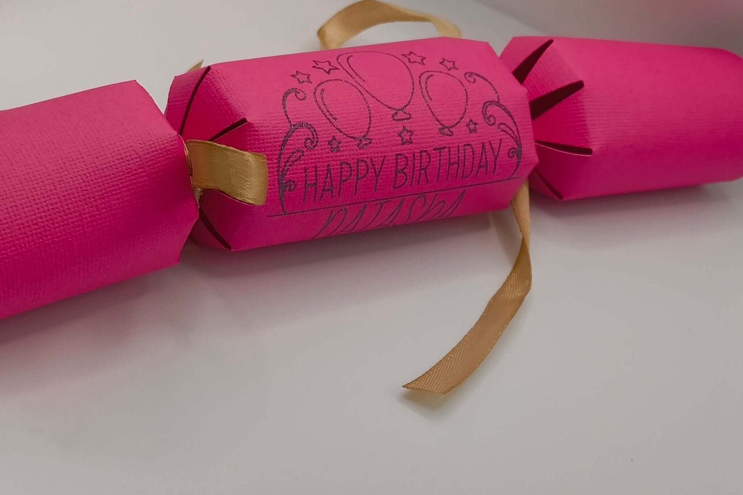 Personalised Birthday Crackers in vibrant pink with happy birthday design and gold ribbon details.