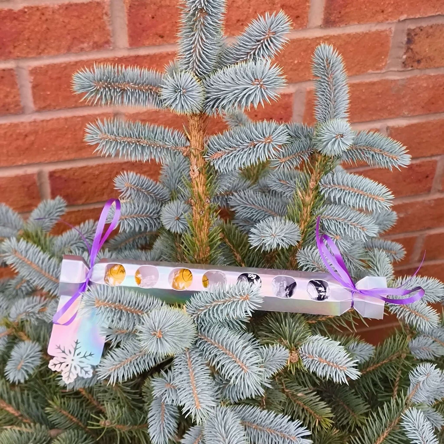 Personalised chocolate cracker gift hanging on a Christmas tree with festive decorations.