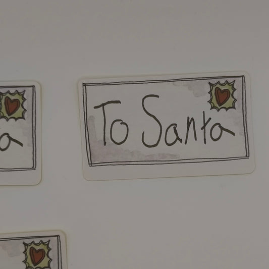 Close-up of To Santa sticker with holly and heart design, festive label style