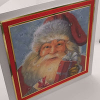 Angled view of a traditional Father Christmas Advent Calendar with numbered doors and gold trim, featuring a vintage Santa holding a red gift, displayed standing upright on a white background.