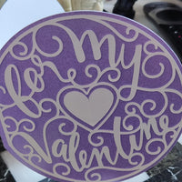 Round handmade Valentine’s card in lilac and cream with an intricate heart and swirled “For My Valentine” cut-out design, shown close-up to highlight detail and texture.
