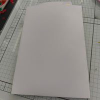 White handmade envelope for wedding money holder, plain cardstock with tab closure, shown flat on craft mat.