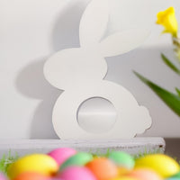 White Easter bunny chocolate holder box with circular cutout, minimalist design with colorful Easter eggs in foreground and yellow flower on the side