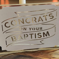 Handmade white cardstock greeting card with gold foil lettering reading 'Congrats on Your Baptism', featuring a cut-out banner design on textured paper