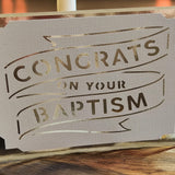 Handmade white cardstock greeting card with gold foil lettering reading 'Congrats on Your Baptism', featuring a cut-out banner design on textured paper