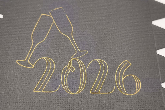Detailed view of gold foiled “2026” with champagne glasses design on black cracker card.