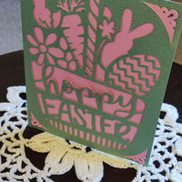 Easter greeting card featuring pink cut-out design with flowers, bunny, and eggs, celebrating springtime joy.