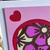 Close-up of a handmade Mother's Day card featuring a floral heart cut-out in pink and purple shades.