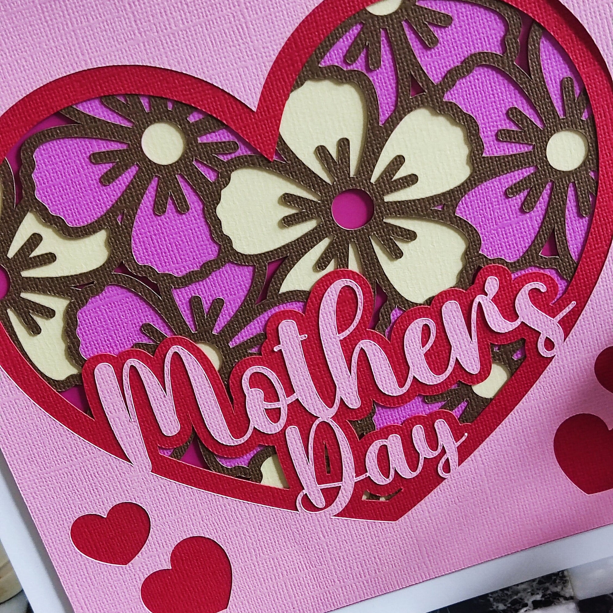 Handmade Mother's Day card with floral heart design in pink and purple, featuring cut-out flowers and layered hearts.