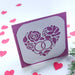 Handmade wedding or anniversary card with a sparkly purple background and a white die-cut floral heart design with wedding rings.


