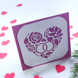 Handmade wedding or anniversary card with a sparkly purple background and a white die-cut floral heart design with wedding rings.


