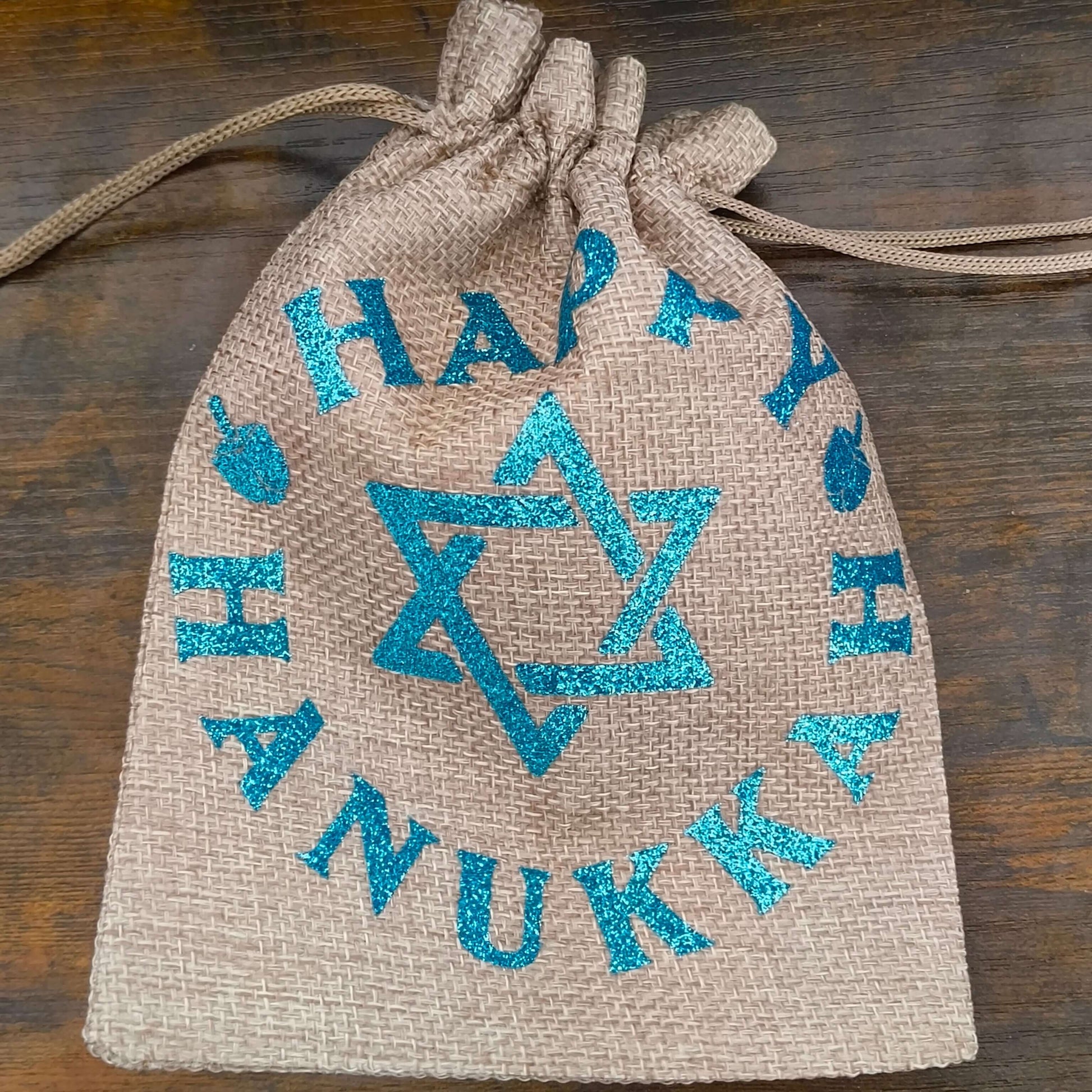 Drawstring Hanukkah hessian bag cinched at top with visible blue glitter Star of David and lettering